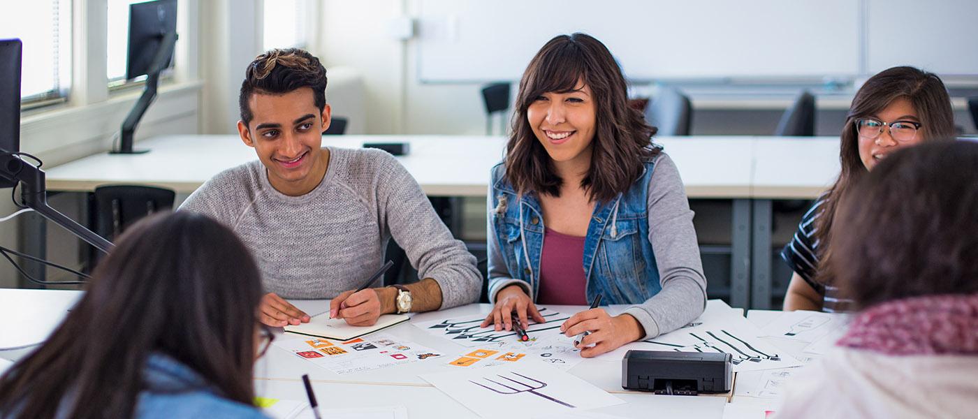 Smiling Graphic Design students in class having a conversation as they look over their projects